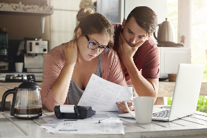 Female in glasses and brunette man studying paper form bank while managing domestic budget together in kitchen interior