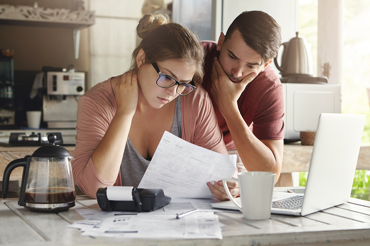 Female in glasses and brunette man studying paper form bank while managing domestic budget together in kitchen interior Female in glasses and brunette man studying paper form bank while managing domestic budget together in kitchen interior