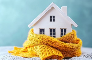 Miniature house wrapped in a warm yellow scarf on a blue background, symbolizing rising electricity prices, higher heating bills, and growing household energy costs