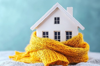 Miniature house wrapped in a warm yellow scarf on a blue background, symbolizing rising electricity prices, higher heating bills, and growing household energy costs