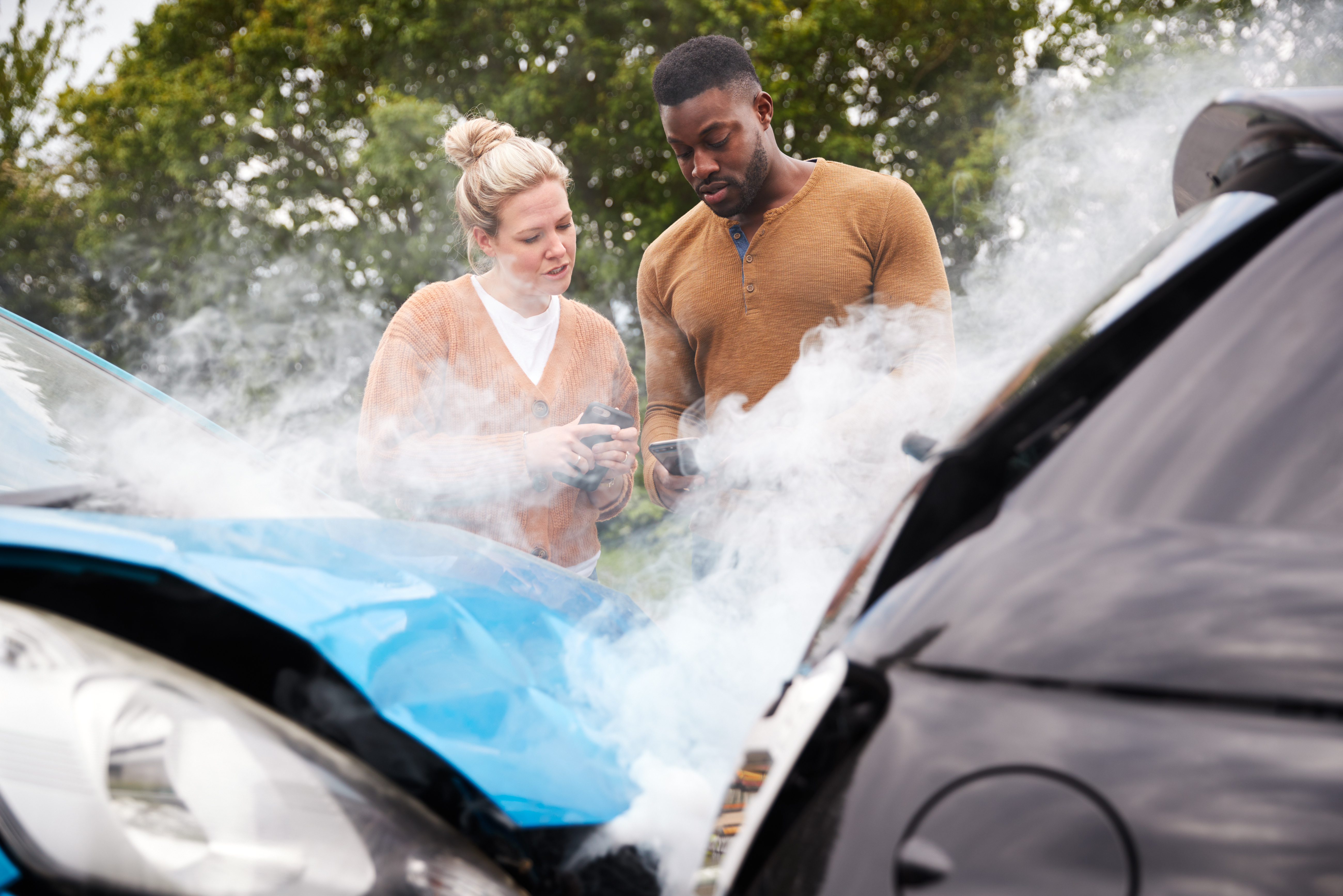 Man and women looking at phones in front of two crashed cars