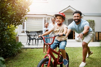 Man pushing boy on bike with woman and girl in background