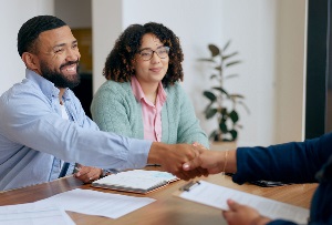 Couple in blue button down and green sweater shaking hands with mortgage officer during signing.