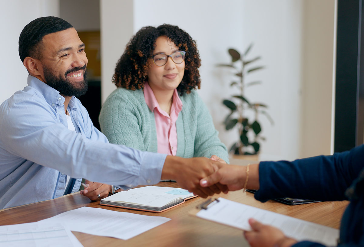 Couple in blue button down and green sweater shaking hands with mortgage officer during signing.
