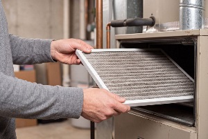Technician replacing dirty air filter inside residential hvac furnace unit in basement. Homeowner performing preventive maintenance for heating system efficiency and clean air.