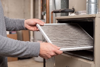 Technician replacing dirty air filter inside residential hvac furnace unit in basement. Homeowner performing preventive maintenance for heating system efficiency and clean air.