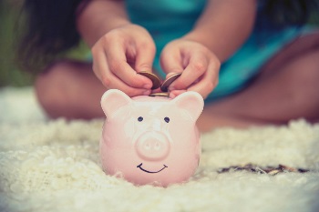 little girl putting coins into a piggy bank