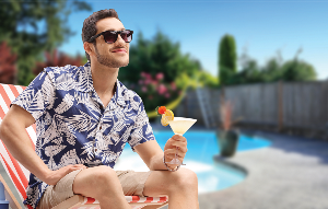 Man in shirt with tropical leaves and tan shorts holding a fun summer drink with garnish Man in shirt with tropical leaves and tan shorts holding a fun summer drink with garnish