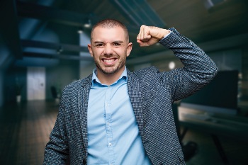 Man in a blue button down and suit jacket flexing