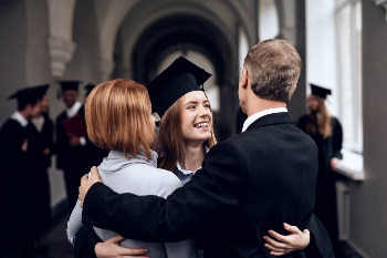 Young woman graduating and hugging her mother and father in her cap and gown