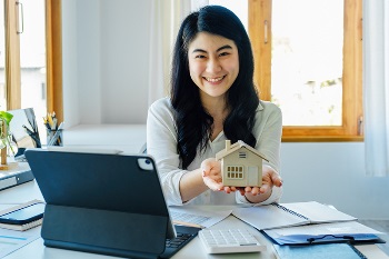 Women holding home model in front of laptop with bills