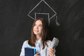 Young girl standing against chalkboard with grad cap drawn, holding cash