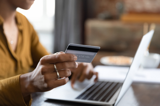 Women at computer holding debit card in yellow cardigan