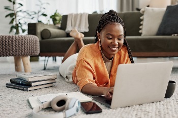 young woman in orange laying on ground with her laptop and electronics surrounding her