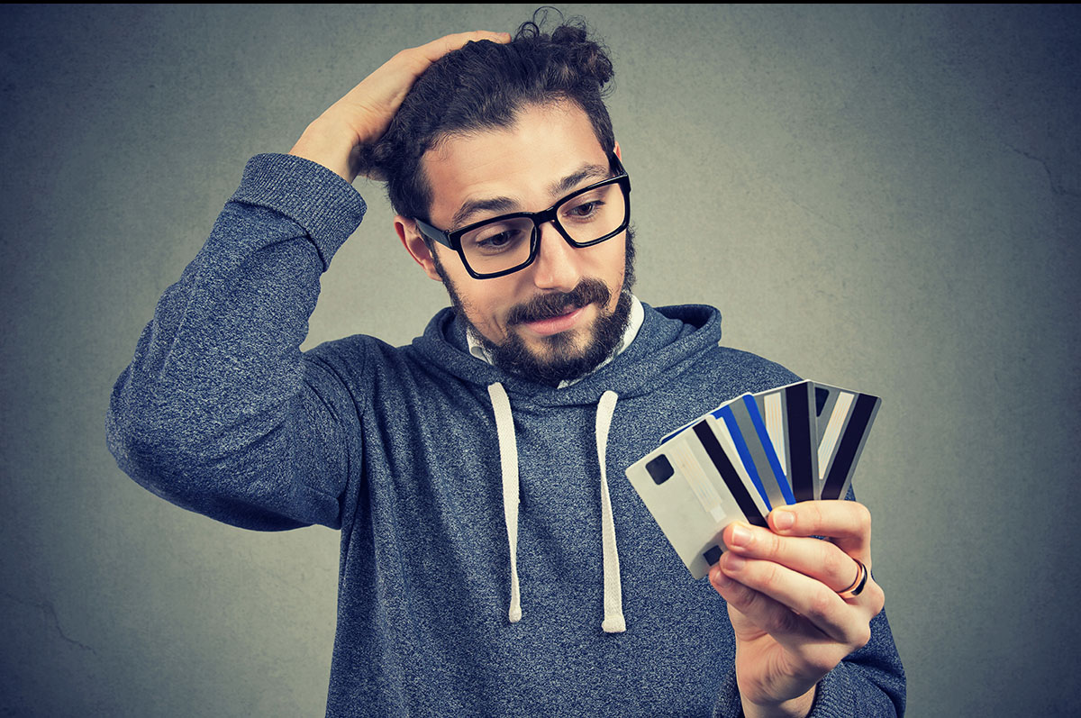 Young man in glasses holding credit cards and looking stressed with increasing debt