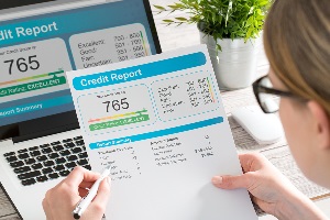 Woman sitting at computer review paperwork with 765 credit score