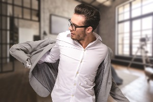 White guy with glasses putting on his grey suit jacket over his white button down