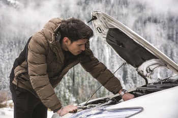 Guy looking under his car hood in the winter