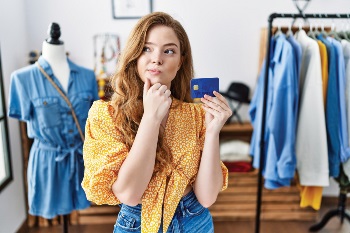Woman at clothing store holding up her credit card, looking puzzled