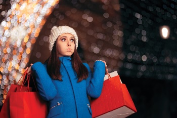 Younger girl with a lot of shopping bags with holiday lights in the background