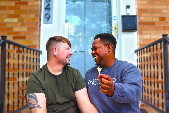 Couple sitting on their doorstep with their house key looking excited towards each other