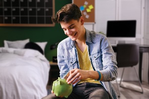 Teenage boy putting money in a piggy bank Teenage boy putting money in a piggy bank