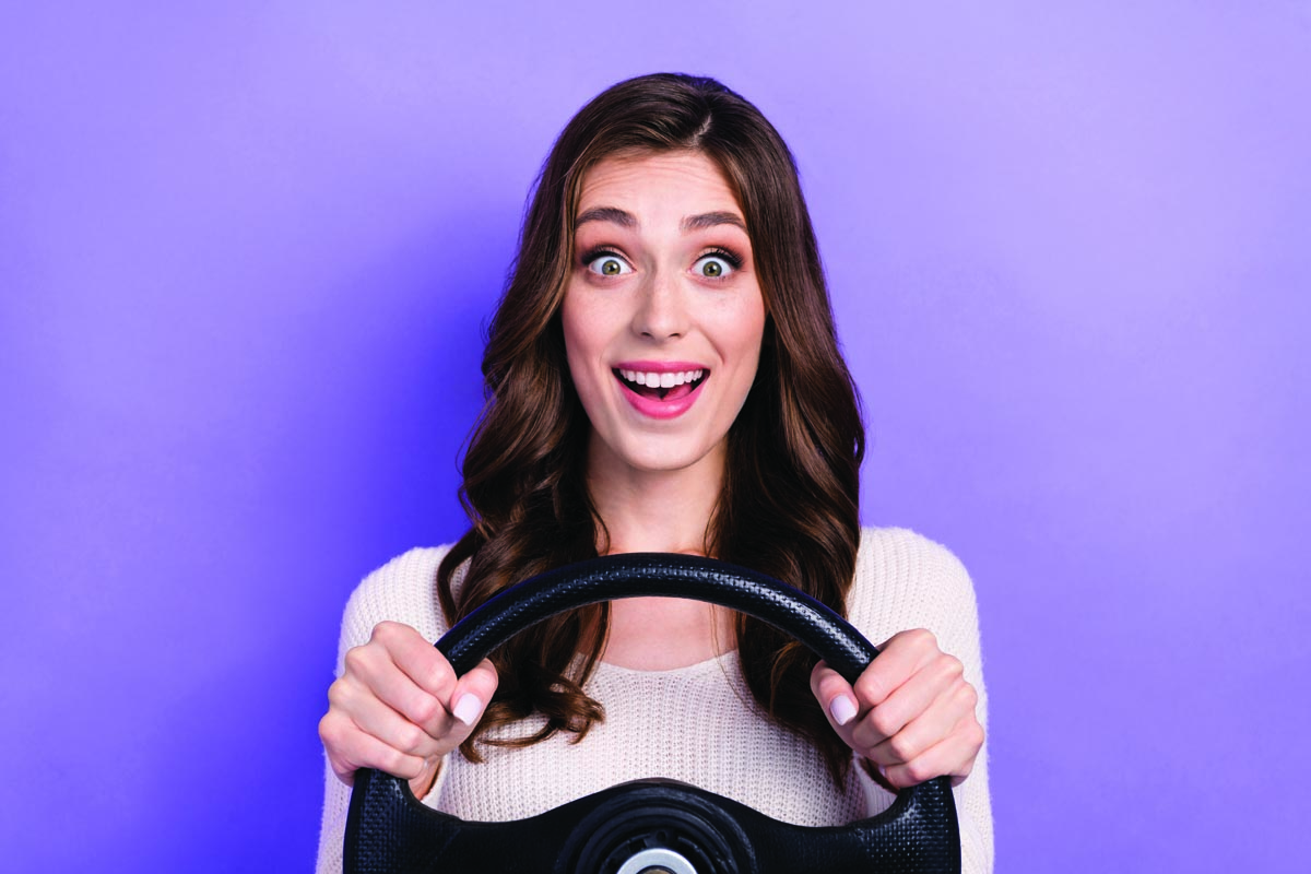 Young woman with her hands on a fake steering wheel with a look of "oh crap"