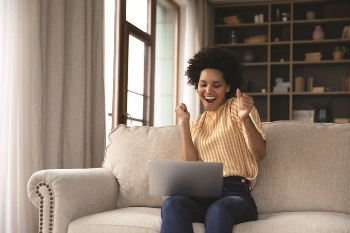 Young woman looking at her laptop in her home and doing a little dance