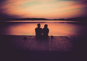 Man and women sitting on a dock looking out onto a sunset