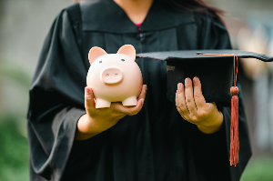 College graduate holding their cap and a piggy bank